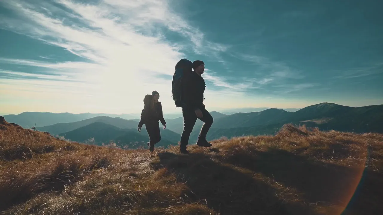 Two walkers with packs crossing a ridge, backlit against the mountains